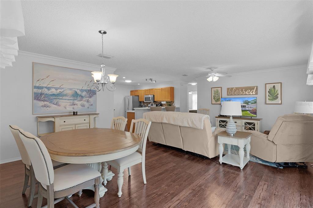 A dining area and living room with wood-look flooring, light-colored furniture, and a kitchen background — 17431 SE 93RD RETFORD TERRACE, THE VILLAGES, FL