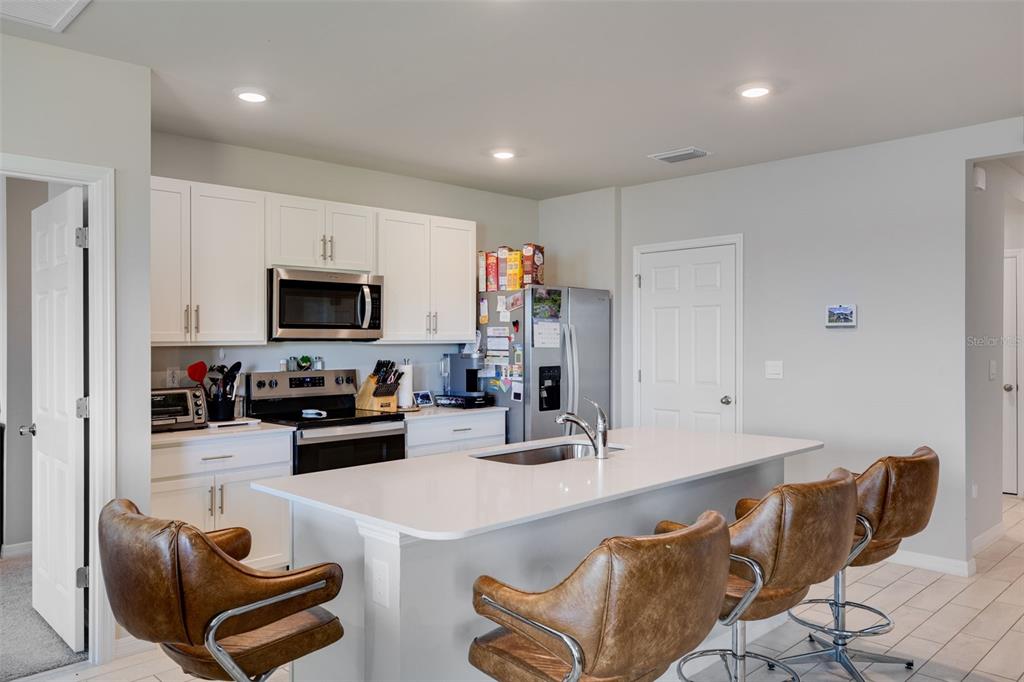 A kitchen features white cabinets, stainless steel appliances, a center island, and brown leather stools — 2608 TABLE CORAL TRAIL, NORTH FORT MYERS, FL