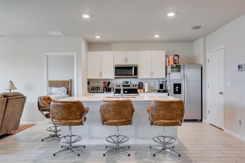 A kitchen features white cabinets, stainless steel appliances, a central island, and three leather stools — 2608 TABLE CORAL TRAIL, NORTH FORT MYERS, FL