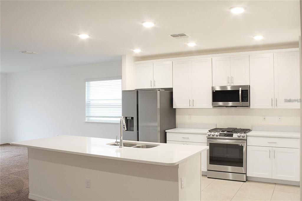 A modern kitchen features white cabinets, stainless steel appliances, and a central island with seating — 1162 OAK BLUFF DRIVE, DAVENPORT, FL
