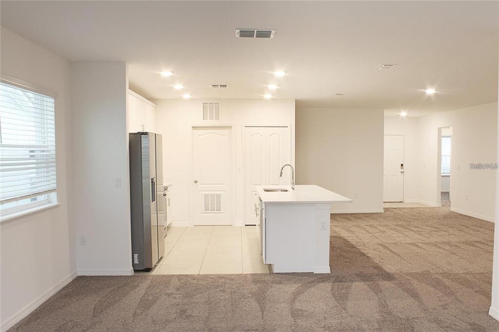A kitchen with white cabinets and an island opens into a carpeted living area — 1162 OAK BLUFF DRIVE, DAVENPORT, FL