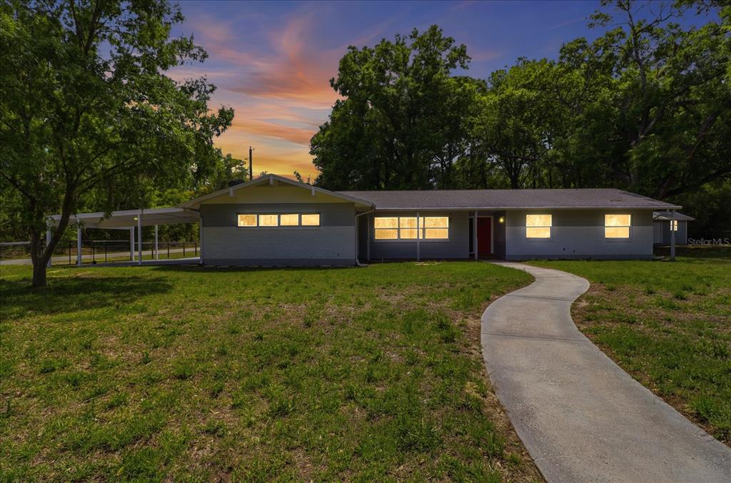 A single-story house with a carport and a curved concrete walkway at dusk — 24576 NW FALCON AVENUE, DUNNELLON, FL