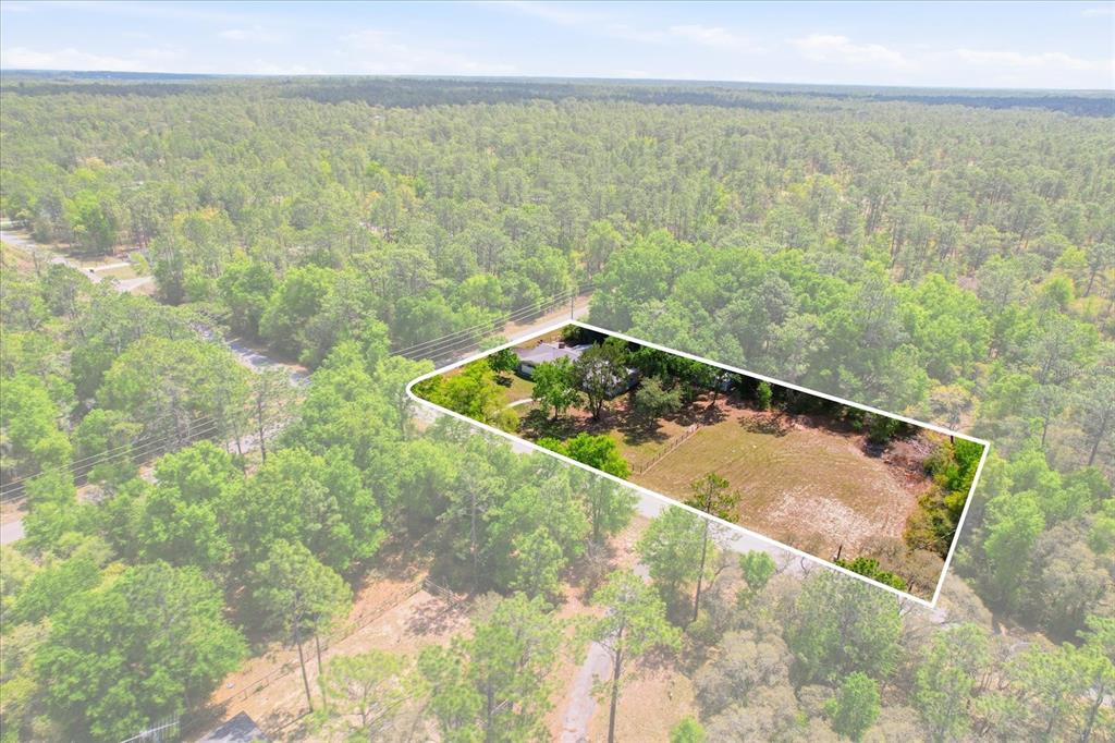 An aerial view shows a house on a large, rectangular lot surrounded by dense forest — 24576 NW FALCON AVENUE, DUNNELLON, FL