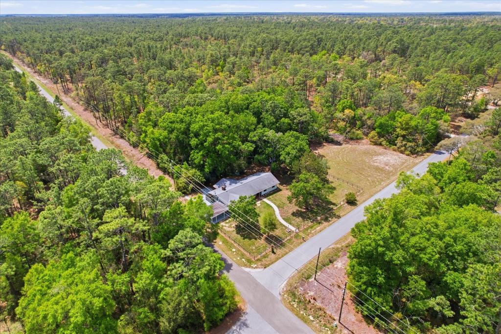 An aerial view shows a house surrounded by dense forest at a rural road intersection — 24576 NW FALCON AVENUE, DUNNELLON, FL