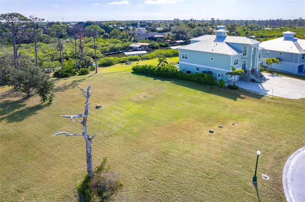 An aerial view shows a large grassy lot next to a multi-story house near water — 8089 WEYERS COURT, ENGLEWOOD, FL