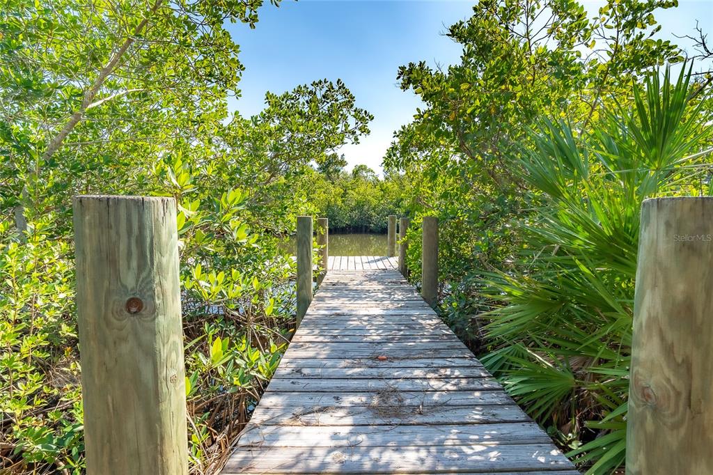 A wooden dock leads through lush green mangroves toward a calm body of water — 8089 WEYERS COURT, ENGLEWOOD, FL