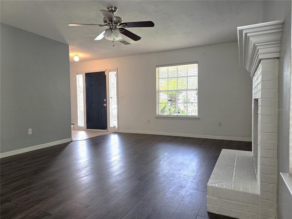 A living room features dark wood-look flooring, a white brick fireplace, and a ceiling fan — 2509 NW 37TH PLACE, GAINESVILLE, FL