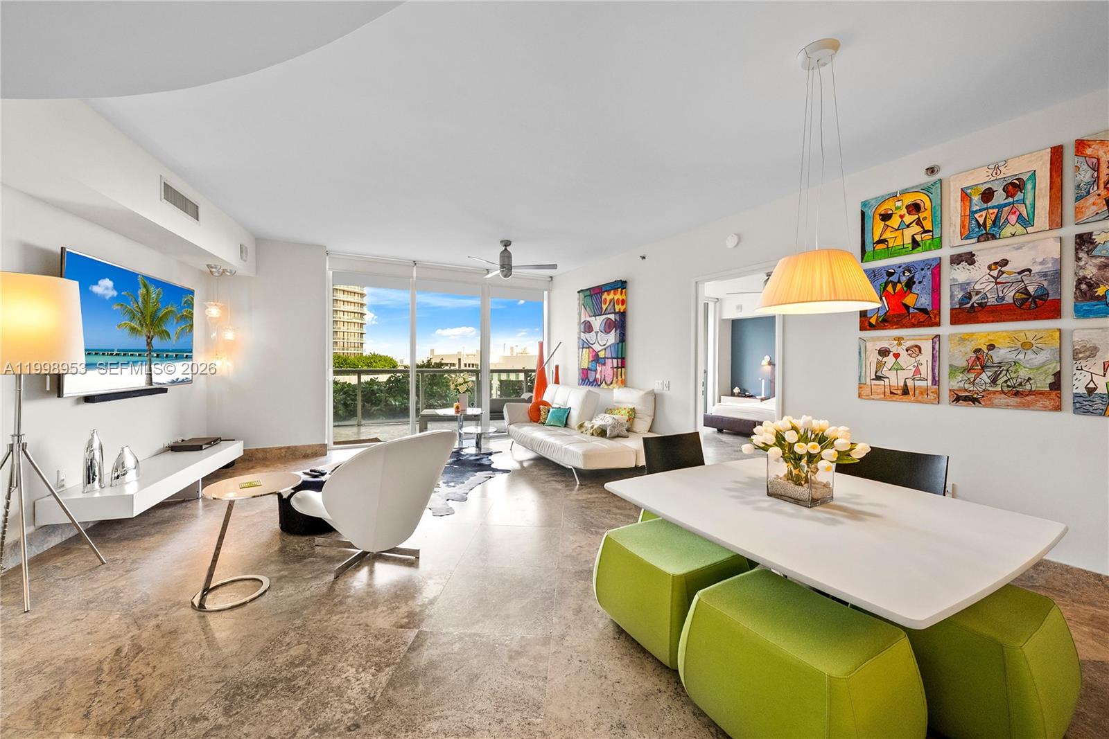 A modern living and dining area features tile floors, colorful wall art, and a balcony — 450 Alton Rd # 704, Miami Beach FL 33139, MIAMI BEACH, FL