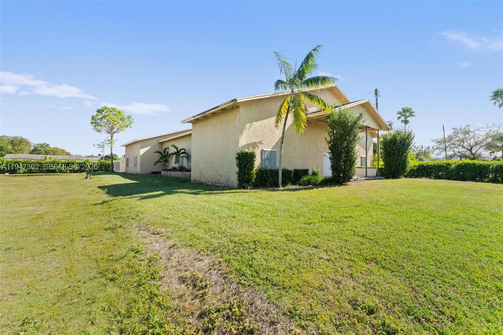 A tan, single-story house sits on a large, grassy lot under a clear blue sky — 21571 SW 110th Ave, Miami FL 33189, MIAMI, FL