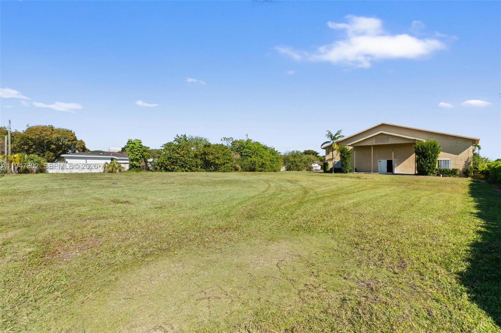 A large, grassy vacant lot sits in front of a tan building under a blue sky — 21571 SW 110th Ave, Miami FL 33189, MIAMI, FL