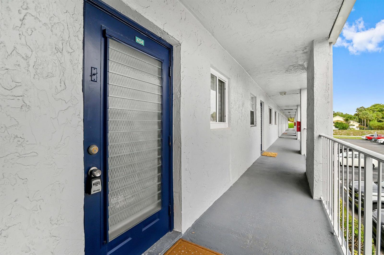 An exterior walkway leads past a blue door labeled 404 toward a parking lot — 2860 SW 22nd Avenue # 4040, Delray Beach FL 33445, DELRAY BEACH, FL