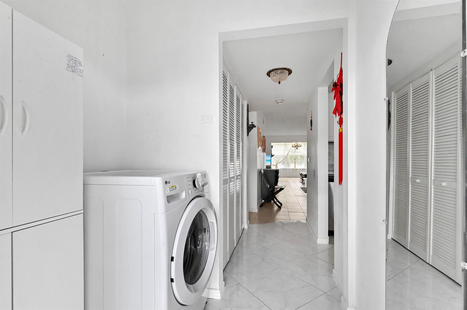 A white front-loading washing machine sits in a hallway with white tile floors and closets — 2860 SW 22nd Avenue # 4040, Delray Beach FL 33445, DELRAY BEACH, FL