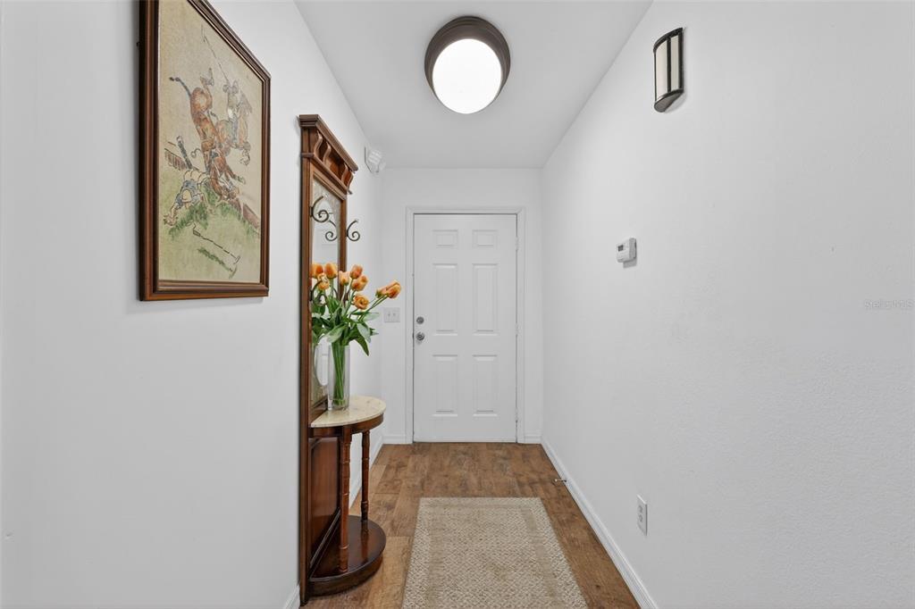 An entryway features a white door, wood-look flooring, a wall-mounted mirror, and a ceiling light — 2296 18TH AVE SW, VERO BEACH, FL
