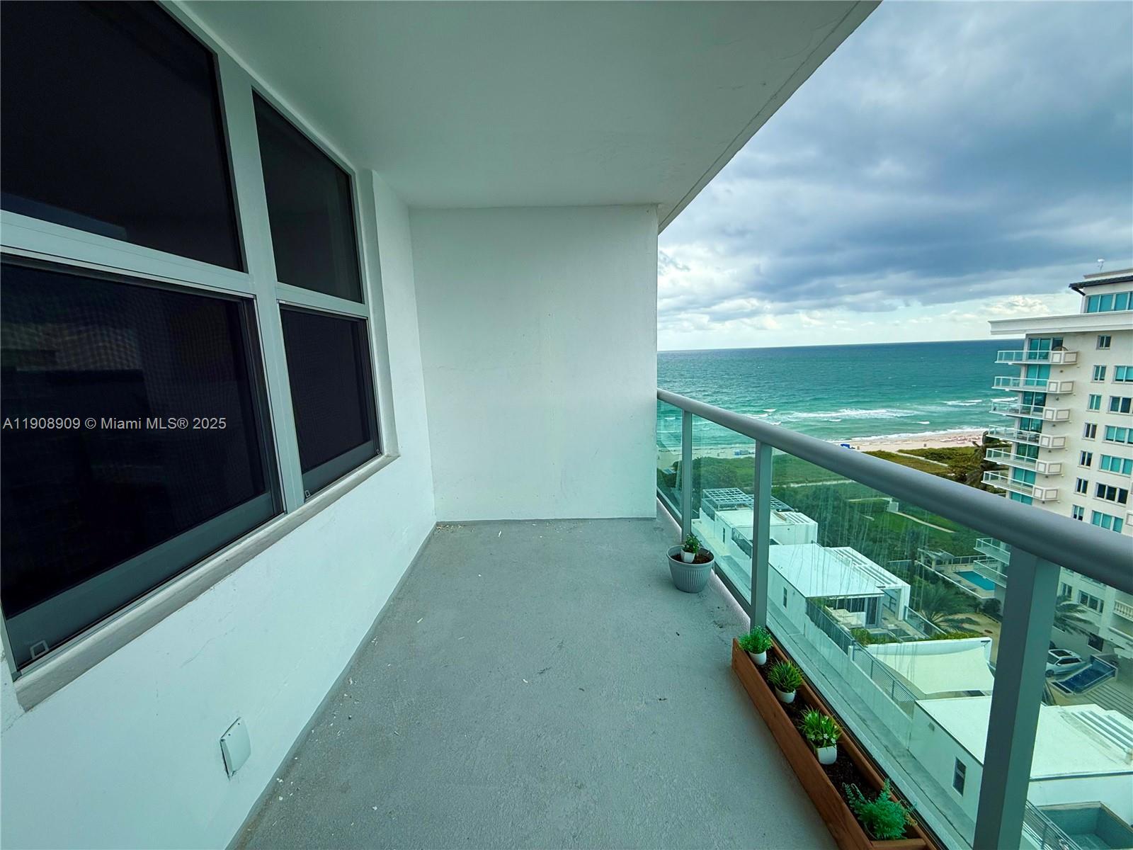 A balcony with a glass railing overlooks the ocean and a neighboring building — 9511 Collins Ave # 1208, Surfside FL 33154, SURFSIDE, FL