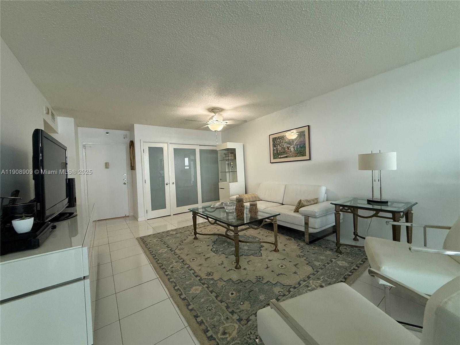 A living room features white tile floors, a glass coffee table, and a white sofa — 9511 Collins Ave # 1208, Surfside FL 33154, SURFSIDE, FL