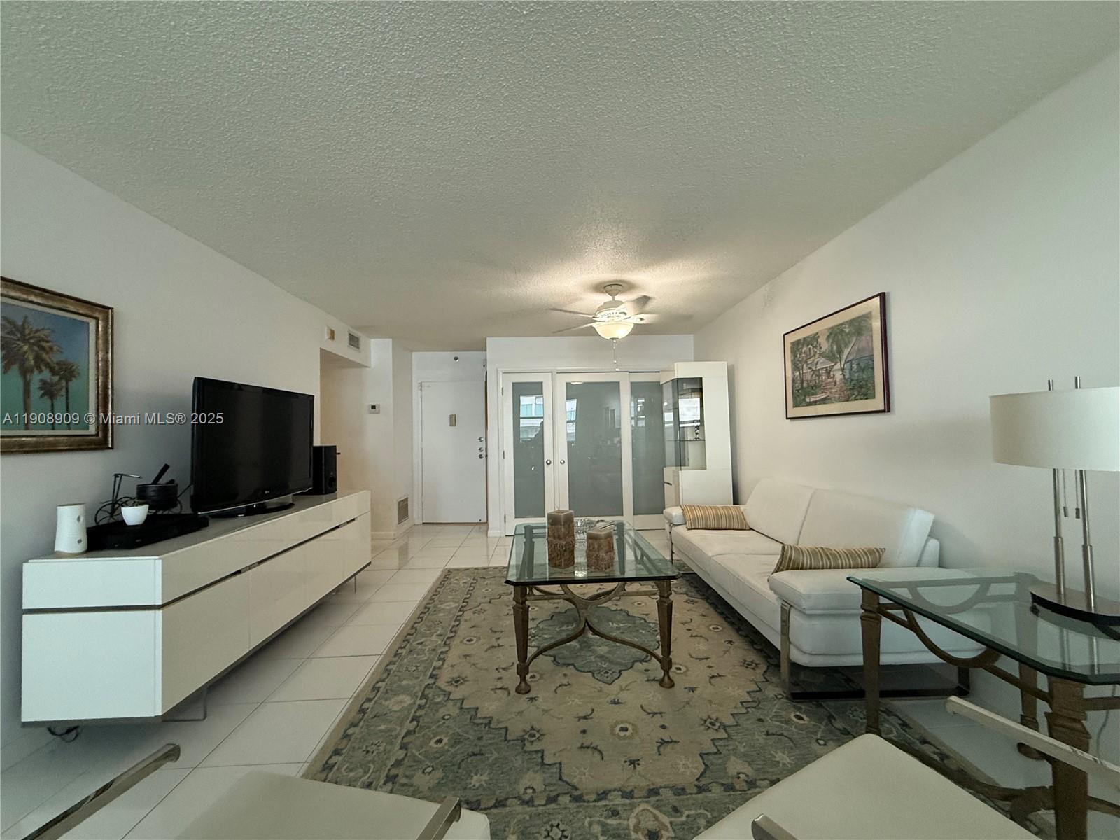 A living room features a white sofa, glass coffee table, media console, and area rug — 9511 Collins Ave # 1208, Surfside FL 33154, SURFSIDE, FL