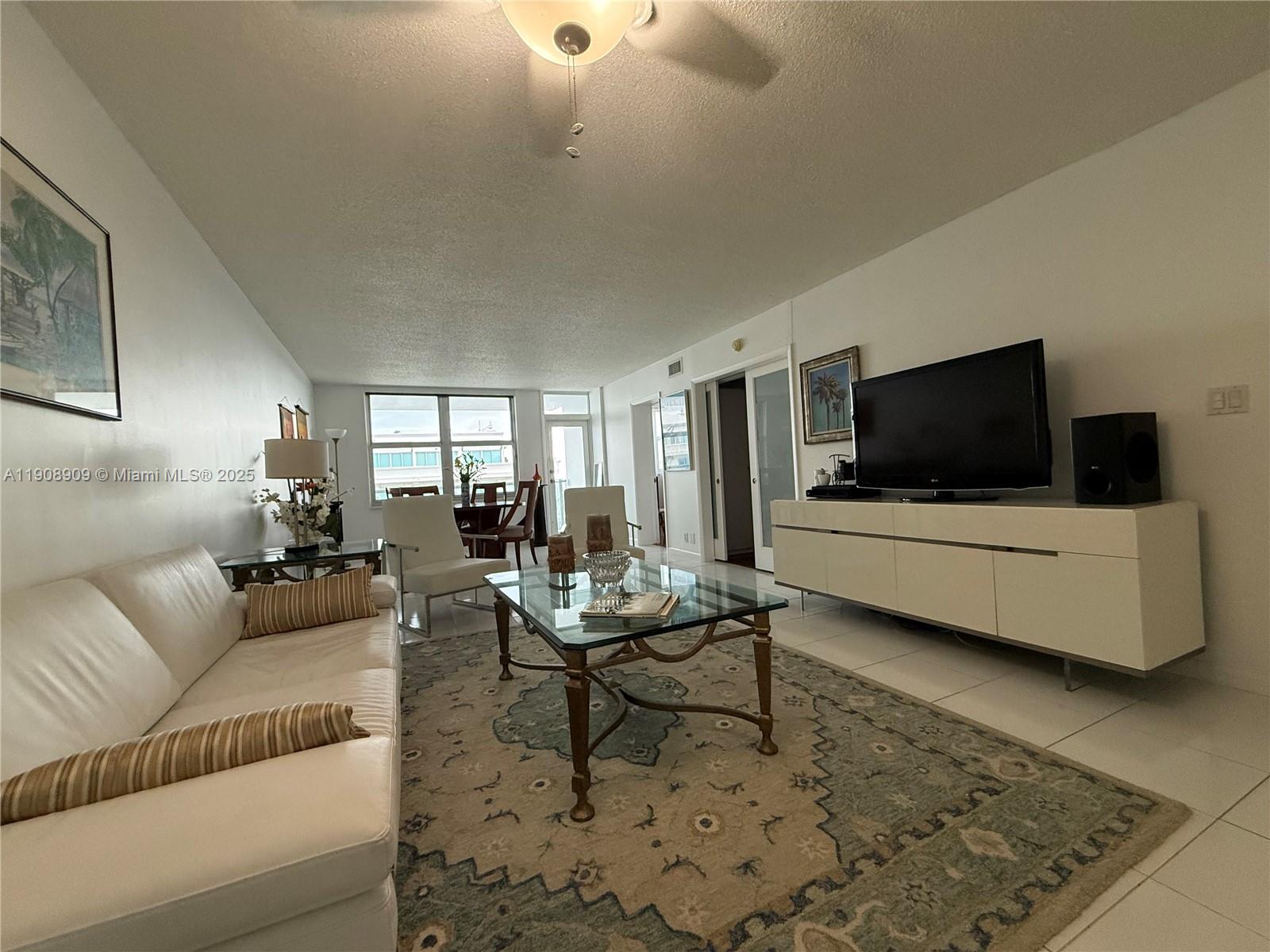 A living room features a white leather sofa, glass coffee table, and a television console — 9511 Collins Ave # 1208, Surfside FL 33154, SURFSIDE, FL