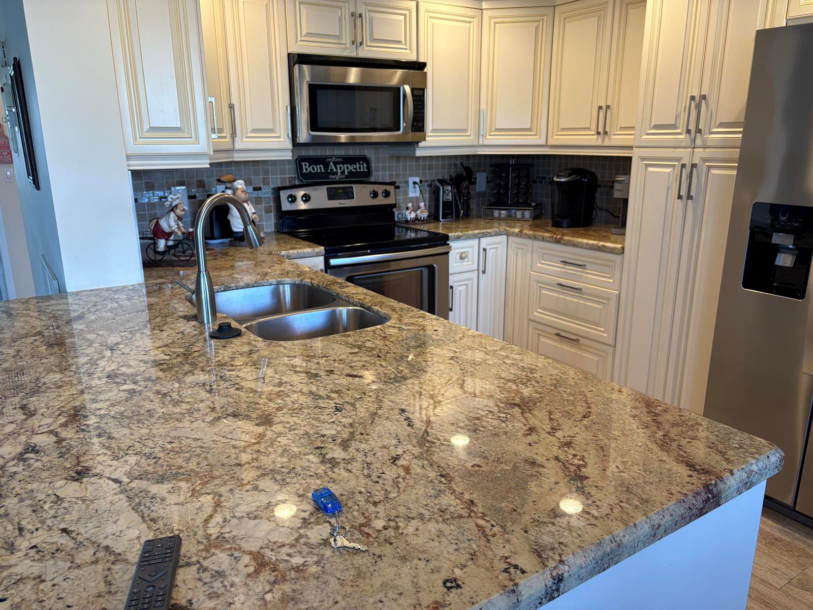 A kitchen features granite countertops, stainless steel appliances, and off-white cabinetry — 2024 Rexford # B, Boca Raton FL 33434, BOCA RATON, FL