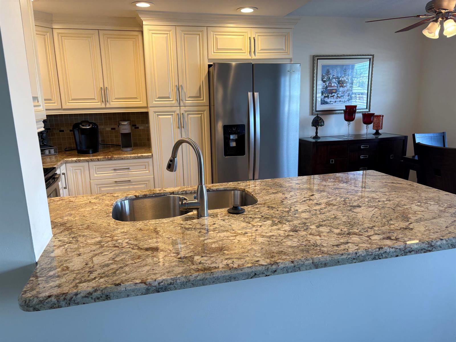 A kitchen features a granite island countertop, stainless steel sink, and cream-colored cabinetry — 2024 Rexford # B, Boca Raton FL 33434, BOCA RATON, FL