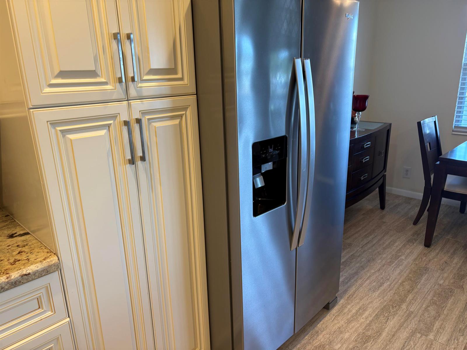 A stainless steel side-by-side refrigerator stands next to white kitchen cabinets with silver handles — 2024 Rexford # B, Boca Raton FL 33434, BOCA RATON, FL