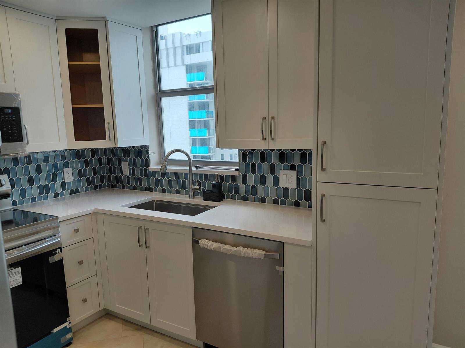 A kitchen features white cabinets, stainless steel appliances, a blue hexagonal tile backsplash, and a window — 1010 S Ocean Boulevard # 1515, Pompano Beach FL 33062, POMPANO BEACH, FL