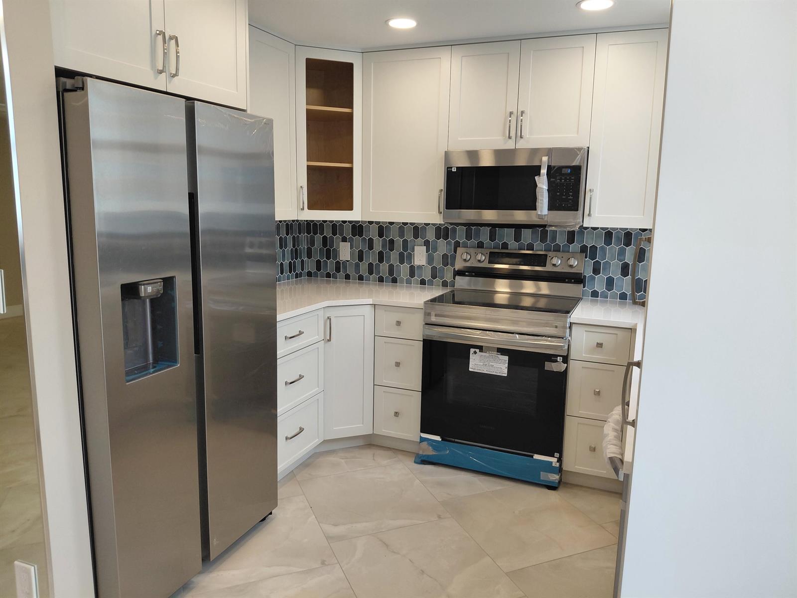 A modern kitchen features white cabinets, stainless steel appliances, and a blue hexagonal tile backsplash — 1010 S Ocean Boulevard # 1515, Pompano Beach FL 33062, POMPANO BEACH, FL