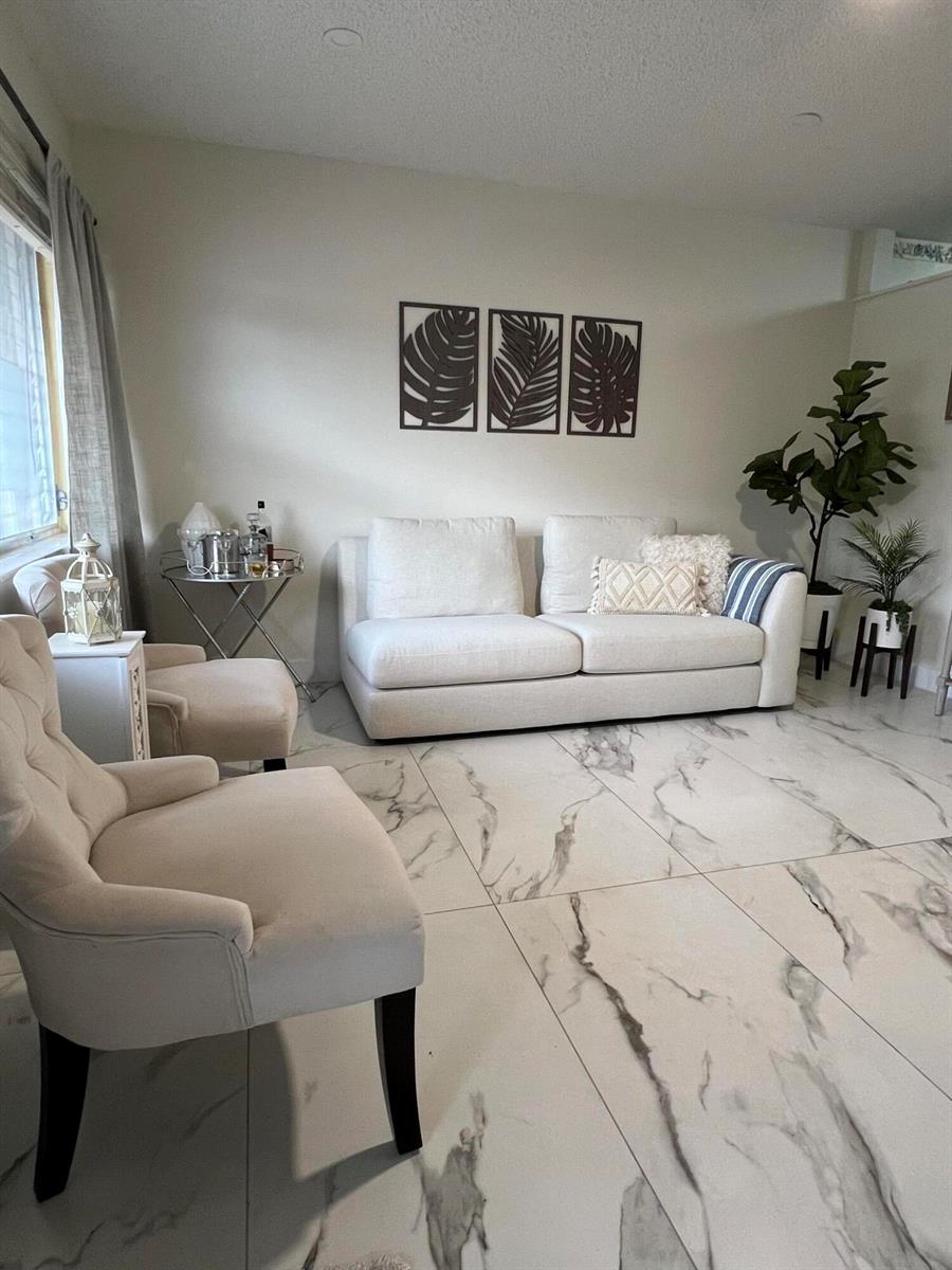 A living room features a white sofa, two armchairs, marble-look tile flooring, and wall art — 900 SW 10th Terrace # S20, Hallandale Beach FL 33009, HALLANDALE BEACH, FL