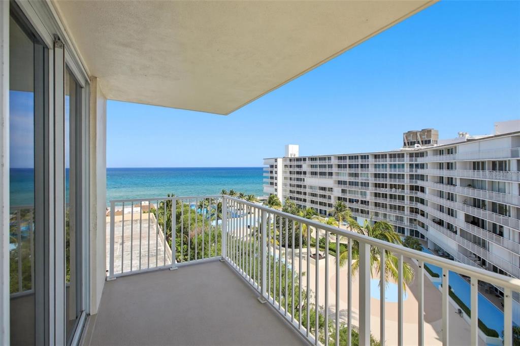 A balcony with white railings overlooks a swimming pool, a large apartment building, and ocean — 3540 S OCEAN BOULEVARD UNIT 808W, PALM BEACH, FL