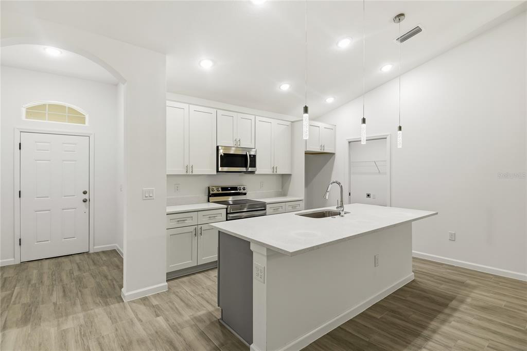 A modern kitchen features white cabinets, stainless steel appliances, a center island, and wood-look flooring — 709 FREDRICK PLACE, KISSIMMEE, FL