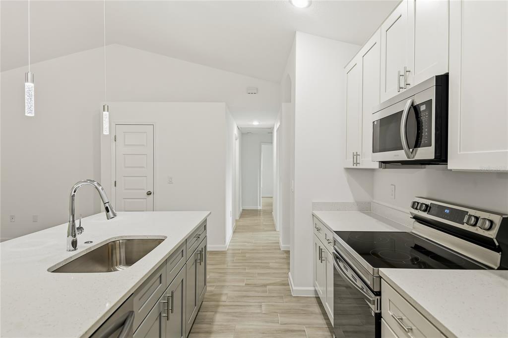 A modern kitchen features a white island with a sink, gray cabinets, and stainless appliances — 709 FREDRICK PLACE, KISSIMMEE, FL