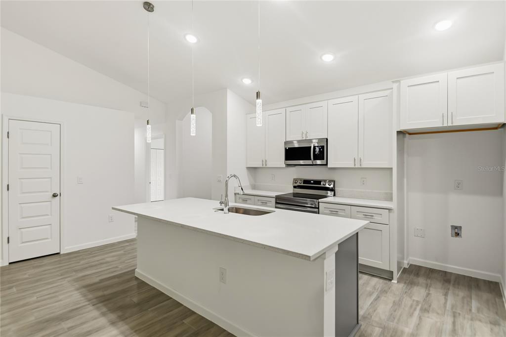 A modern kitchen features white cabinetry, a central island with a sink, and gray flooring — 709 FREDRICK PLACE, KISSIMMEE, FL