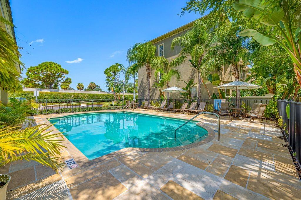 A swimming pool with a stone deck and lounge chairs sits beside a multi-story building — 7125 102ND LANE, SEMINOLE, FL