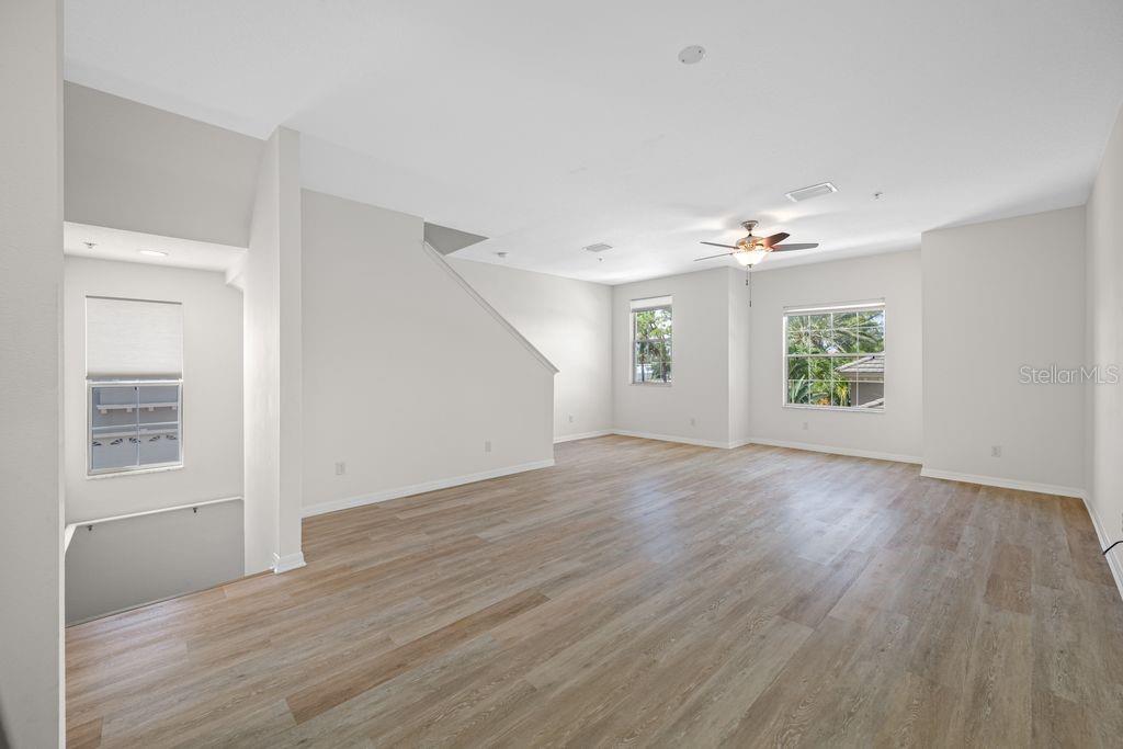 An empty room features light wood-look flooring, white walls, a ceiling fan, and multiple windows — 7125 102ND LANE, SEMINOLE, FL