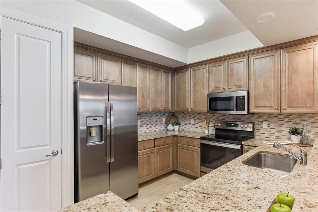 A kitchen with light wood cabinets, granite countertops, stainless steel appliances, and a tiled backsplash — 3 RIVERWALK DRIVE UNIT 404, NEW SMYRNA BEACH, FL