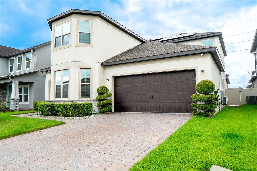 A two-story house with a beige stucco exterior, a brown garage door, and manicured landscaping — 3231 PALATKA STREET, ORLANDO, FL