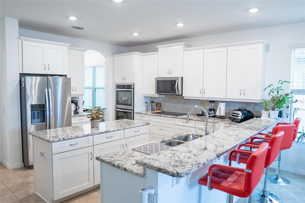 A kitchen features white cabinets, granite countertops, stainless steel appliances, and red bar stools — 3231 PALATKA STREET, ORLANDO, FL