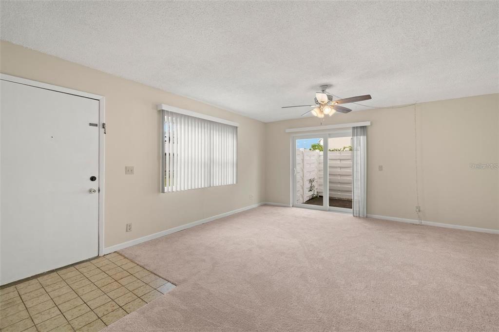A living room features beige carpet, a ceiling fan, a sliding glass door, and blinds — 3247 38TH WAY S UNIT C, ST PETERSBURG, FL