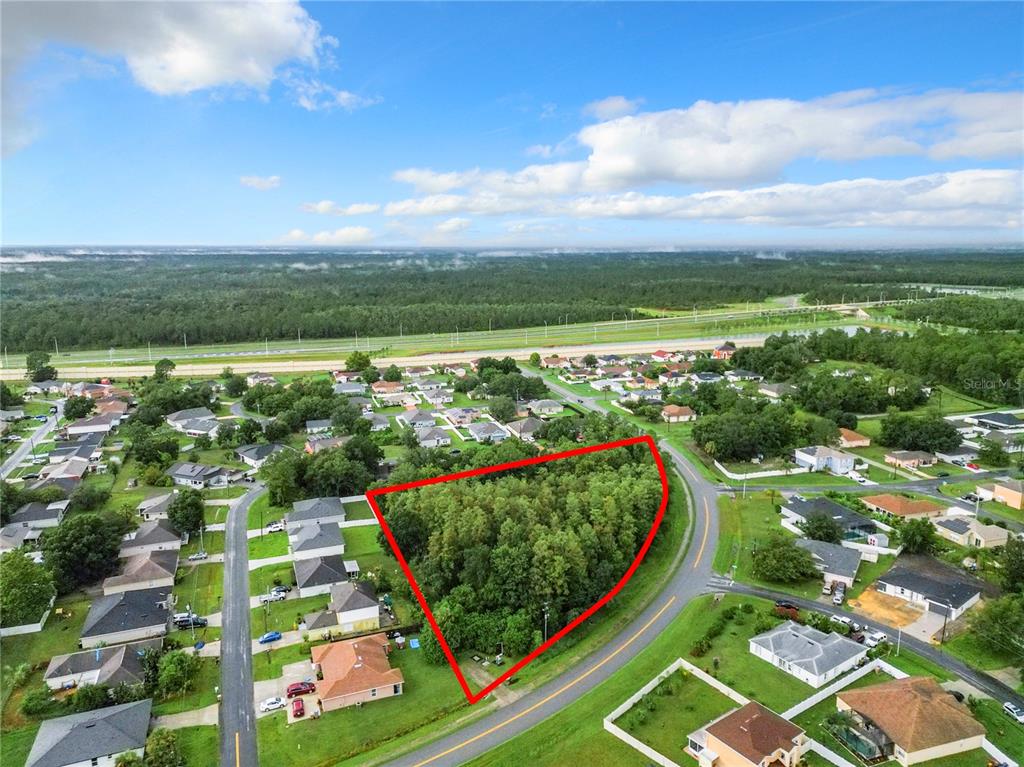 An aerial view shows a triangular, wooded vacant lot surrounded by suburban houses and roads — 0 PEABODY ROAD, KISSIMMEE, FL