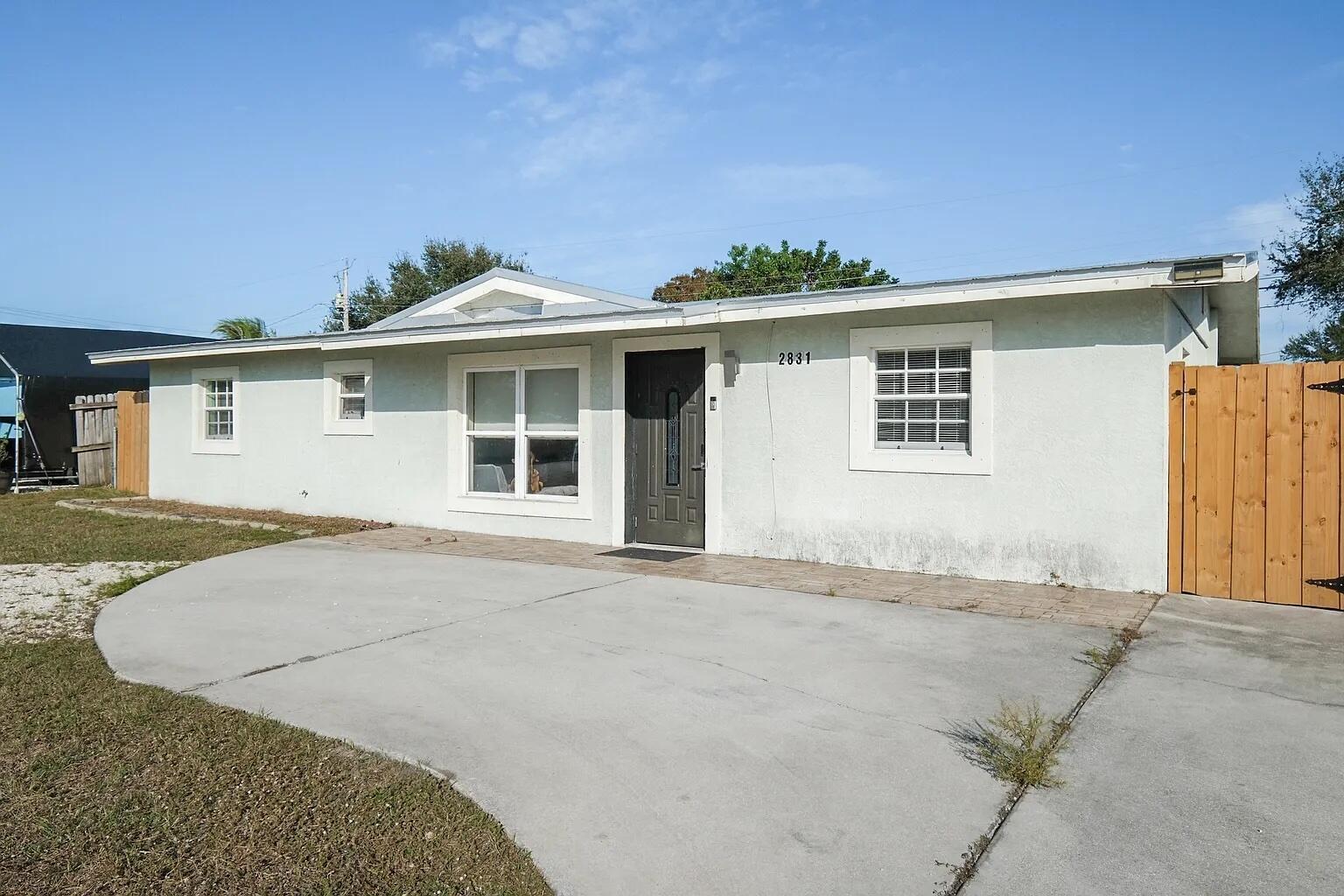 A single-story house with a light-colored stucco exterior, a gray front door, and concrete driveway — 2831 NE Savannah Road, Jensen Beach FL 34957, JENSEN BEACH, FL