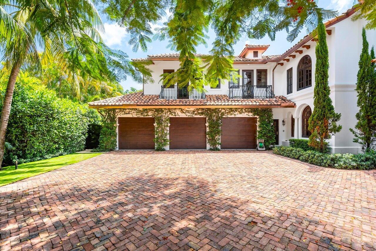 A three-car garage with wooden doors sits beneath a balcony in front of a house — 350 E Ocean Avenue, Lantana FL 33462, LANTANA, FL