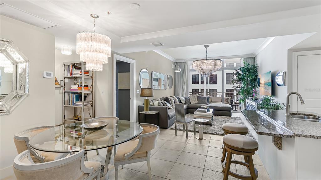 An open-concept living and dining area features tile floors, crystal chandeliers, and a kitchen island — 1350 MAIN STREET UNIT 1503, SARASOTA, FL