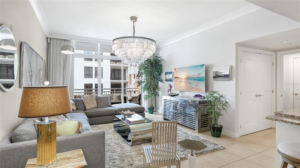 A modern living room features a grey sectional sofa, crystal chandelier, and a large television — 1350 MAIN STREET UNIT 1503, SARASOTA, FL