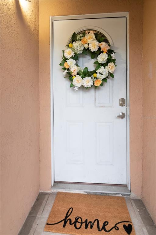 A white front door with a floral wreath and a welcome mat sits in a entryway — 13613 OLD FARM DRIVE, TAMPA, FL