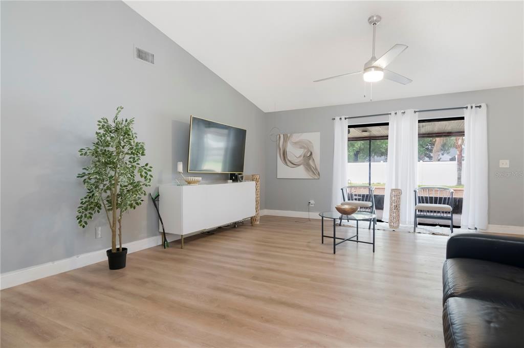 A living room features light wood flooring, a white media console, and a ceiling fan — 13613 OLD FARM DRIVE, TAMPA, FL