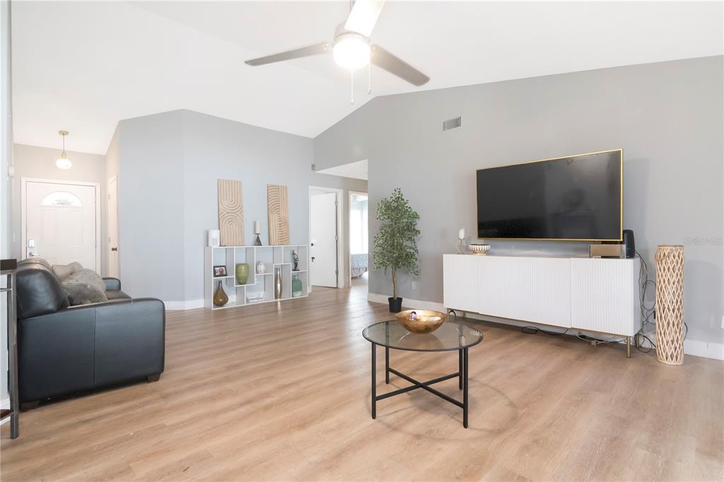 A living room features light wood flooring, gray walls, a ceiling fan, and a television — 13613 OLD FARM DRIVE, TAMPA, FL