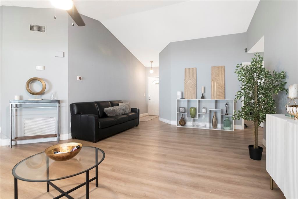 A living room with light wood flooring, a black sofa, and a white shelving unit — 13613 OLD FARM DRIVE, TAMPA, FL