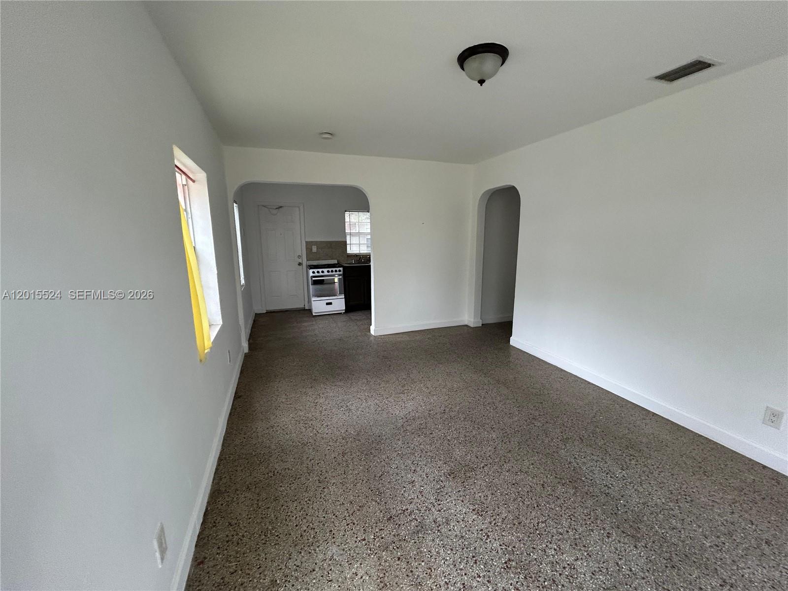 An empty room with white walls, a speckled floor, and an arched kitchen entrance — 2316 Madison St # 19, Hollywood FL 33020, HOLLYWOOD, FL