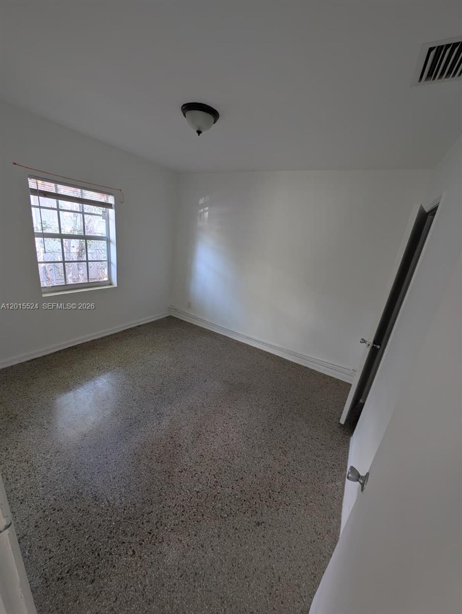 An empty bedroom features white walls, a window, and speckled gray flooring — 2316 Madison St # 19, Hollywood FL 33020, HOLLYWOOD, FL