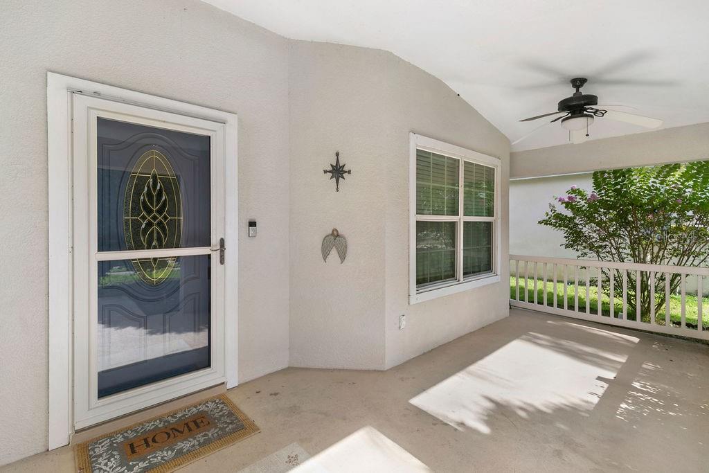 A covered porch features a white front door with a storm door and a ceiling fan — 4511 DERBYSHIRE DRIVE, TITUSVILLE, FL