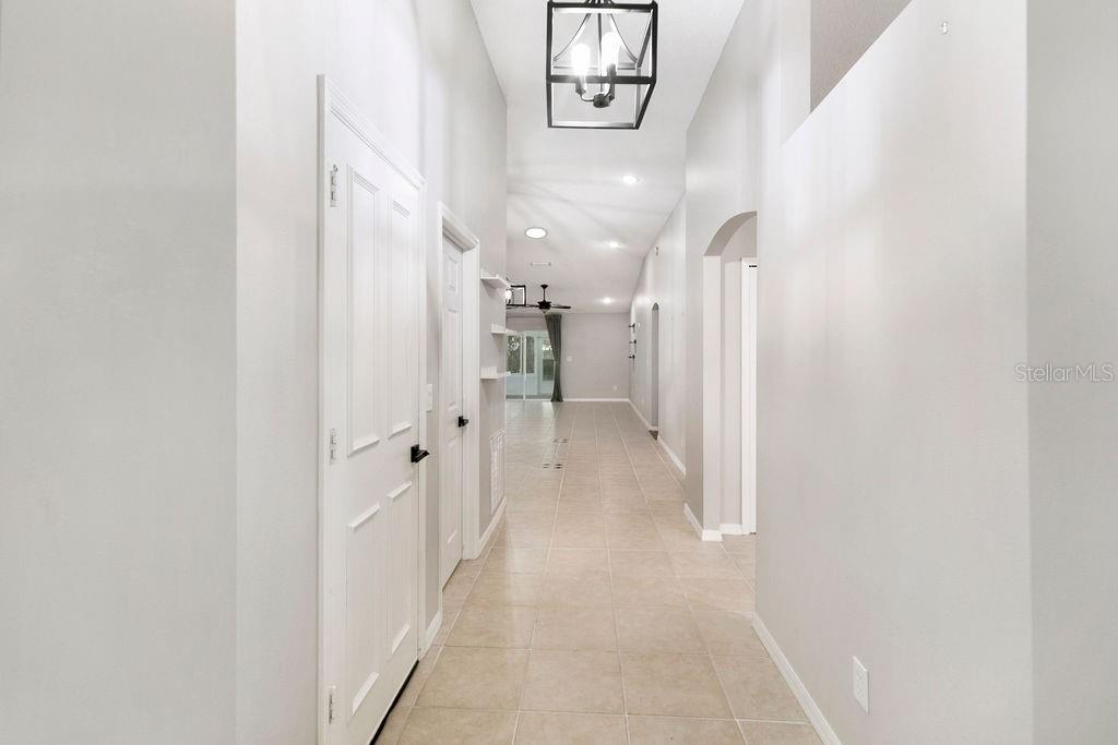 A long hallway with light tile flooring leads toward a bright living area — 4511 DERBYSHIRE DRIVE, TITUSVILLE, FL